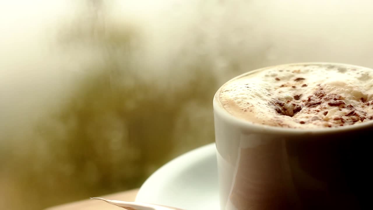 Primo piano di un cappuccino bollente e fumante con scaglie di cioccolato.