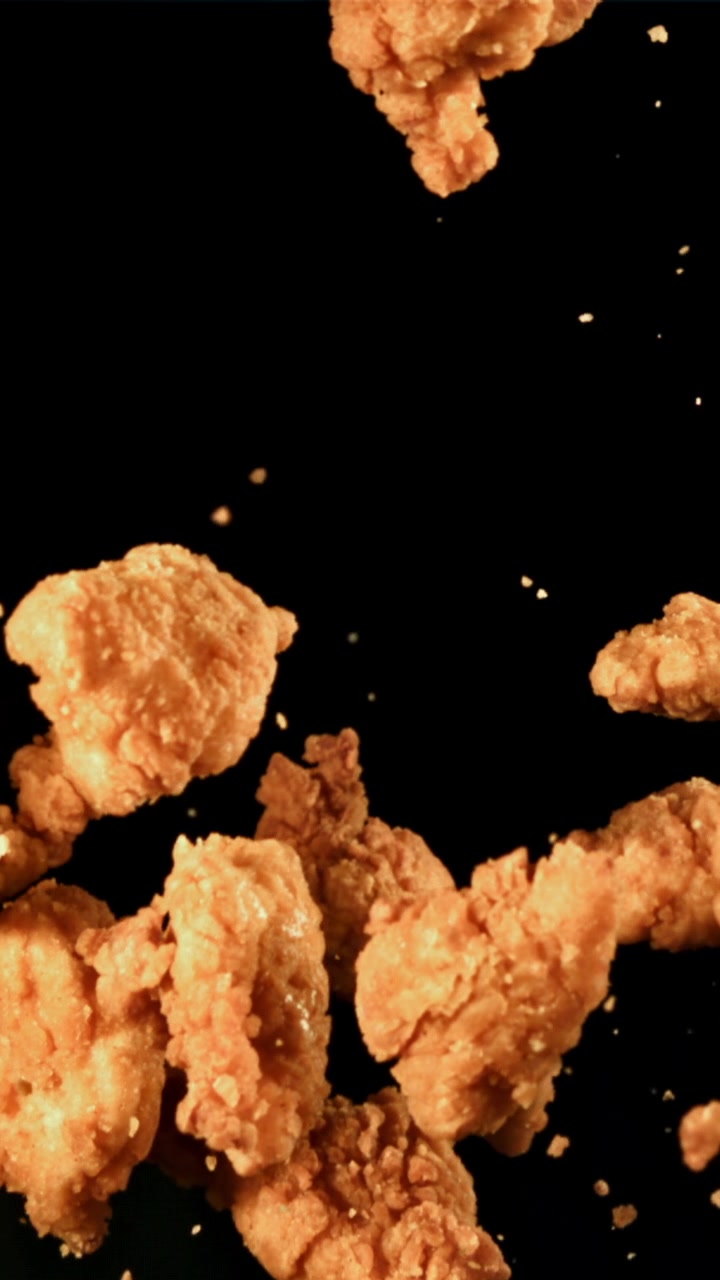 Pezzi di pollo fritto croccante che galleggiano in slow motion su sfondo nero
