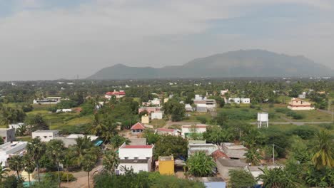 aerial flyover above an indian village surrounded by green trees and huge mountains in the background of the frame