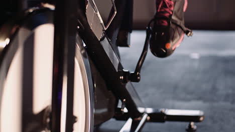 Low-Section-Of-Young-Woman-Exercising-On-Stationary-Bike-At-Health-Club