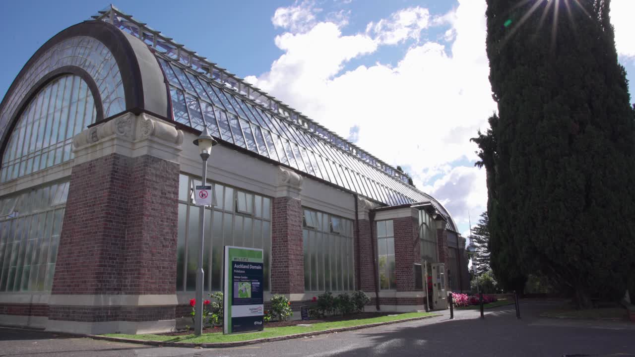 Wide view of the Auckland Domain Winter Gardens greenhouse and Cool House and its glass building on a sunny day
