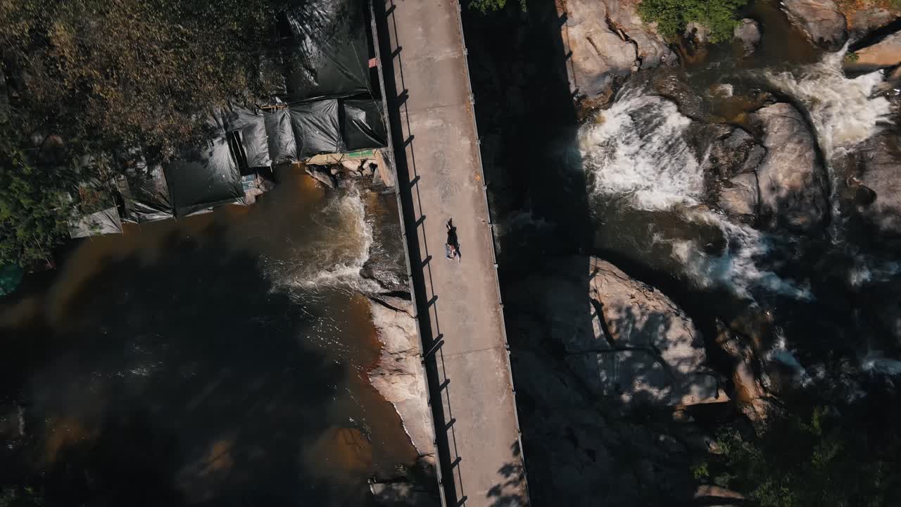 아름다운 금발의 여인은 다리 아래로 물이 흐르면서 태국의 매클랑 폭포 위의 돌다리 위에 놓여 있습니다.