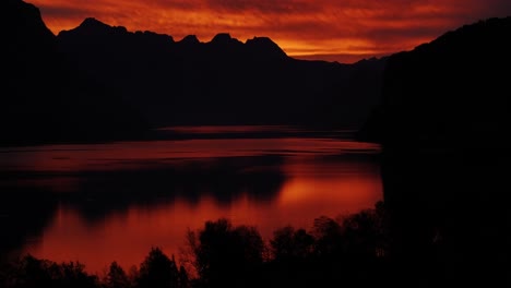 orange sunrise over lake walensee with silhouettes of the swiss alps and their reflections on the water.
