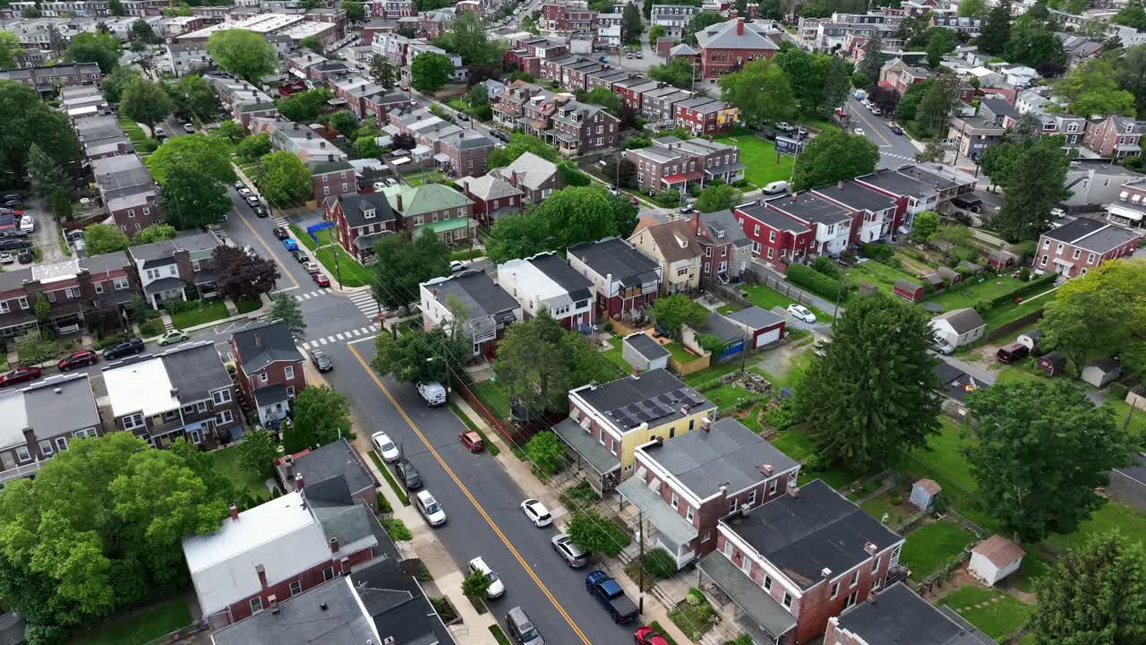 Quartiere americano con una fila di case e abitazioni a due piani in Pennsylvania. Auto parcheggiate in strada e un'auto in transito che attraversa un incrocio. Alberi verdi in primavera con la luce del sole. Ripresa aerea dall'alto.