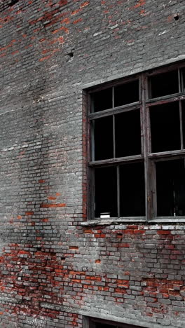 forlorn building with crashed windows. approaching to the brick wall of the construction. industrial chimney pipe at the backdrop. vertical video