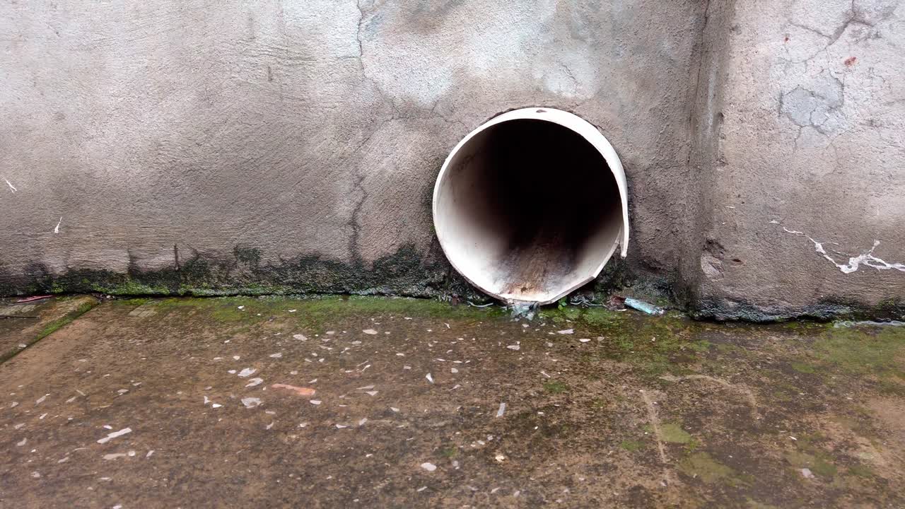 Curved view around a white drainage pipe slowly dripping on concrete wall with moss