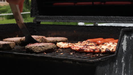 male-hand-flipping-meat-cooking-on-an-outdoor-grill