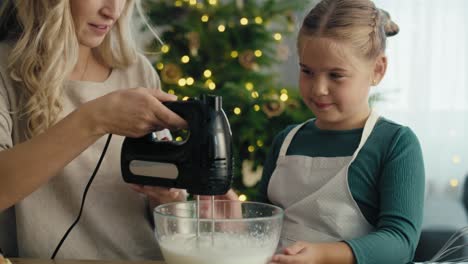 caucasian mother and daughter preparing baking using electric mixer in the kitchen before christmas.