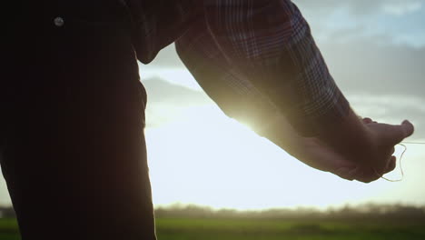 man holding a ball of string unfolds it on the filed, sun is shinning in background, low perspective