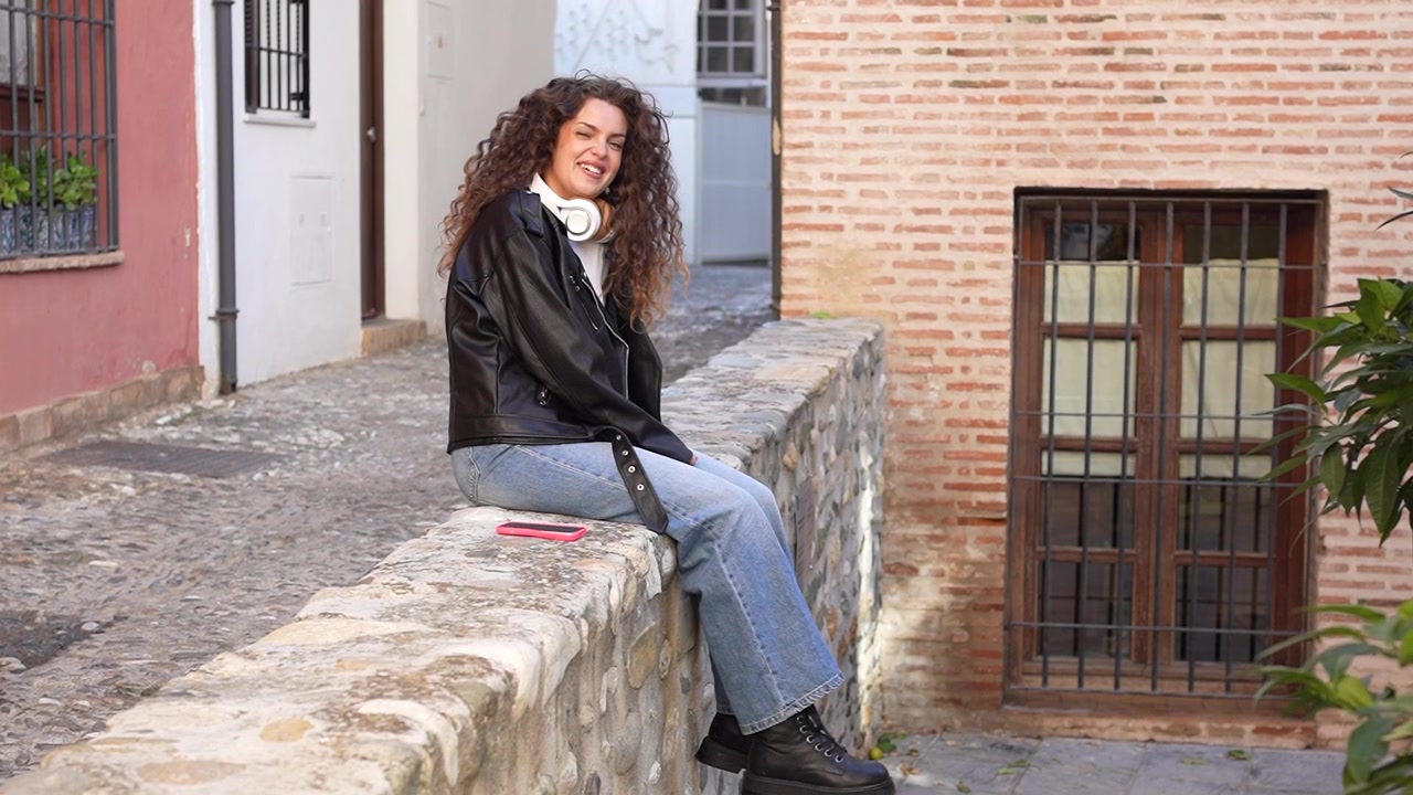 A young woman is enjoying a relaxing moment while sitting on a stone wall in a scenic setting