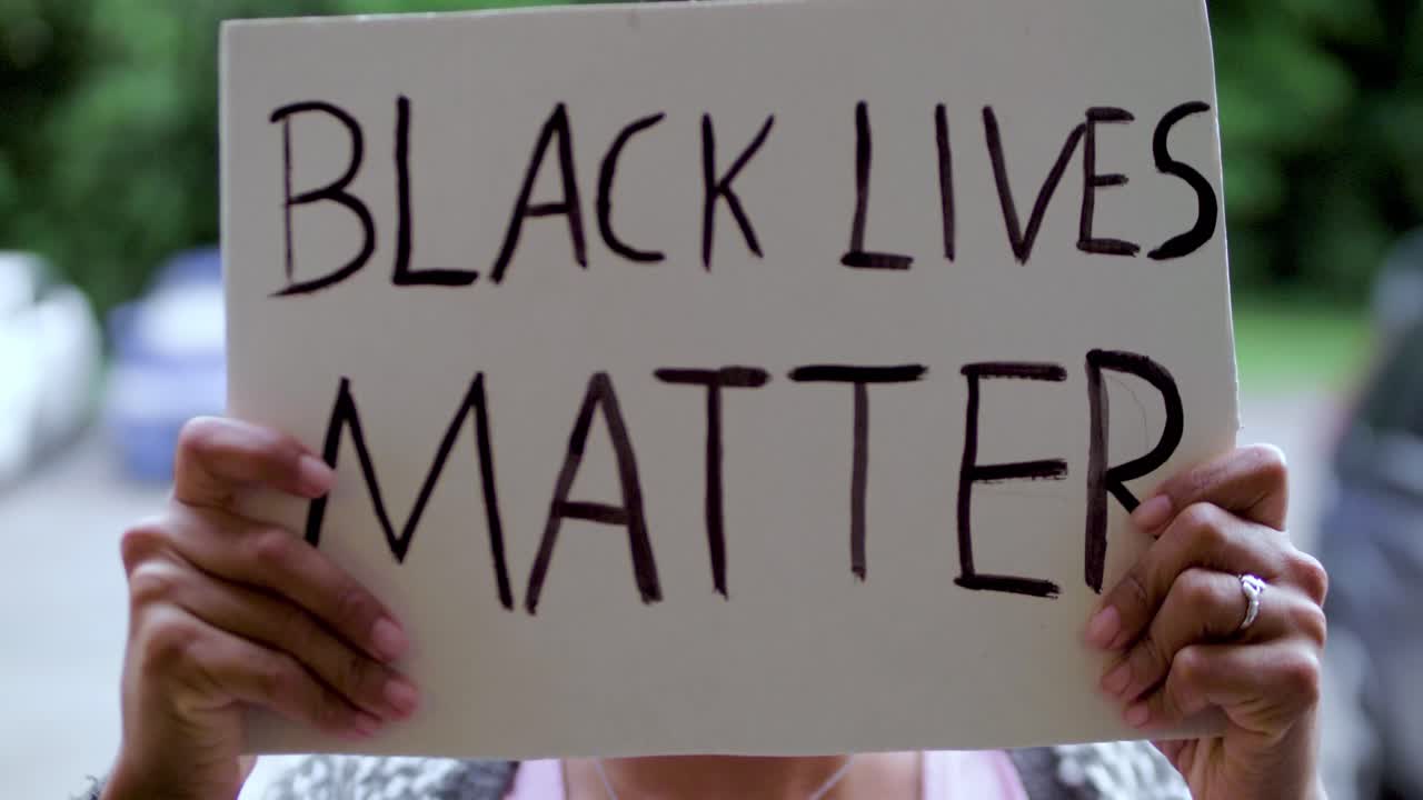 Young black Woman holds a &amp;quot;Black Lives Matter&amp;quot; Poster in front of her Face