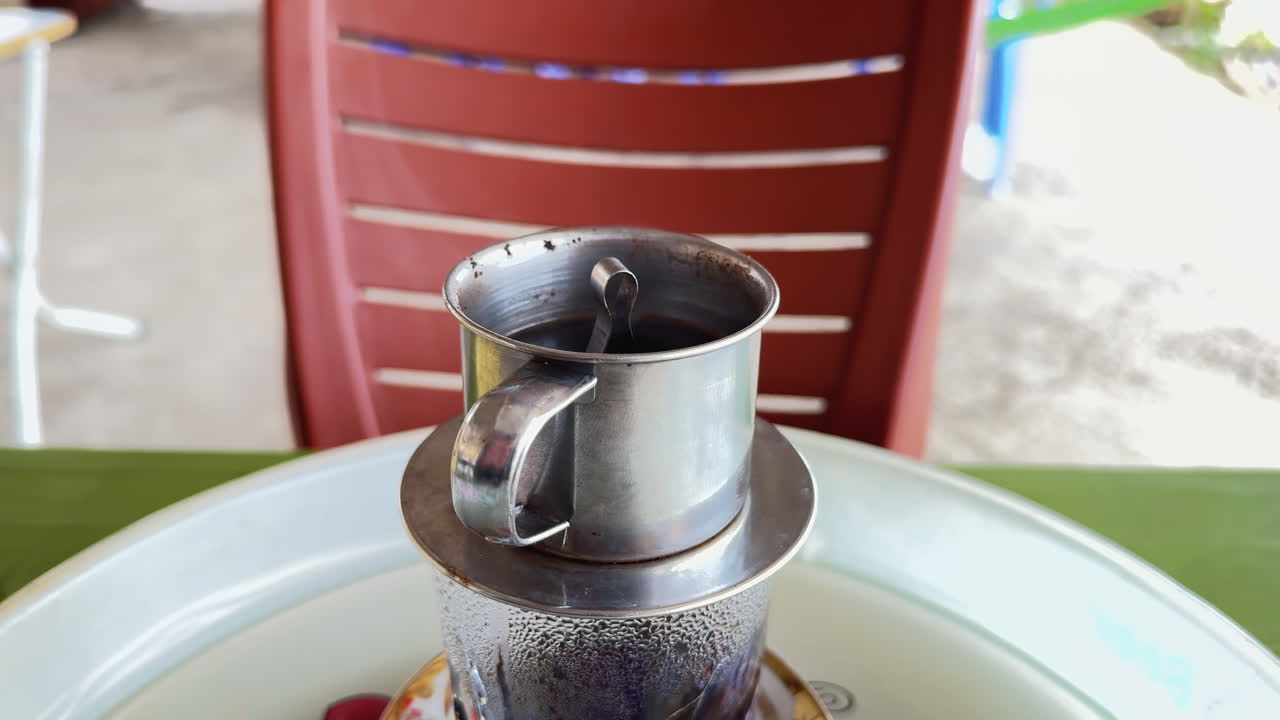 Plum Blossom Valley, Vietnam. Close-up of traditional Vietnamese phin filter brewing coffee, steam rising. Highlights local coffee culture and aromatic experience.