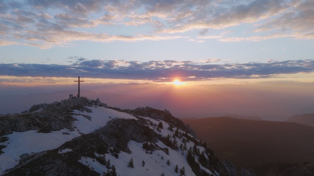 Drone revealing mountain peak at sunset with summit cross and people walking on the ridge