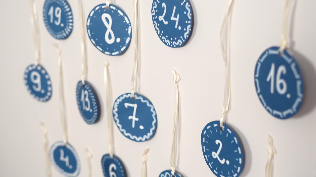 Calendario dell'avvento fatto a mano con cerchi di carta blu e numeri bianchi appesi a dei fili su una parete bianca, decorazioni natalizie minimaliste e festive per il conto alla rovescia