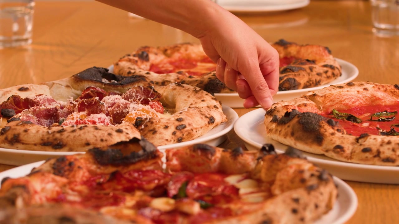 Un cameriere posiziona diverse pizze cotte nel forno a legna su un tavolo di legno in un ambiente accogliente di ristorante.