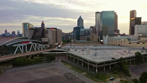 state farm arena with parking area and skyline of atlanta downtown during golden sunrise. aerial approaching wide shot. truist plaza, bank of america plaza and peachtree tower with sunlight in back.