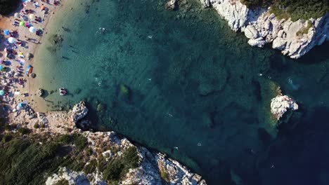 Aerial-shot-of-stunning-wild-beach,-lagoon-and-people-sunbathing-and-swimming-in-ocean