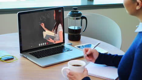 estudiante caucásica usando una computadora portátil en una videollamada con una maestra, tomando notas