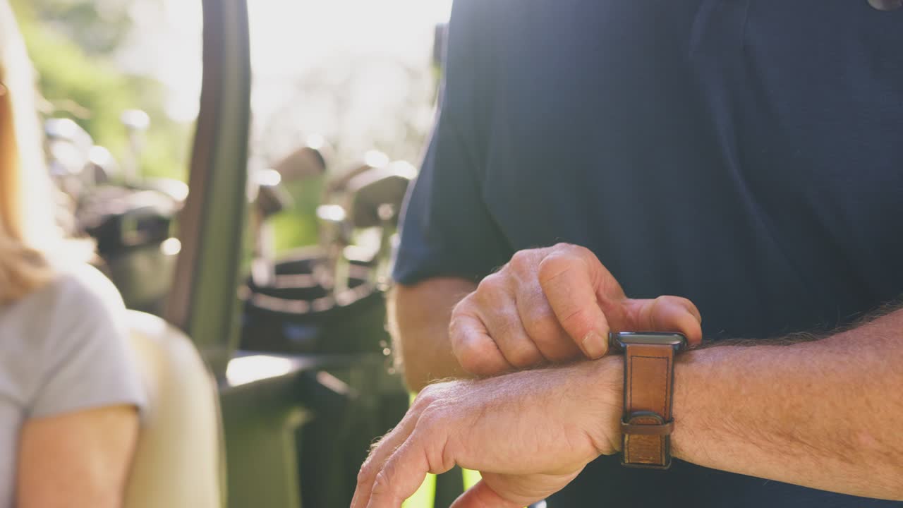 cerca del hombre comprobando reloj inteligente como una pareja madura sentarse en el buggy y jugar una ronda de golf juntos