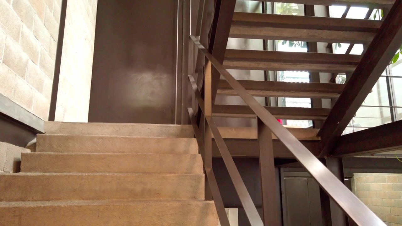 Interior view of a modern concrete staircase with metal railings, exposed structural elements, and contemporary architecture illuminated by natural daylight