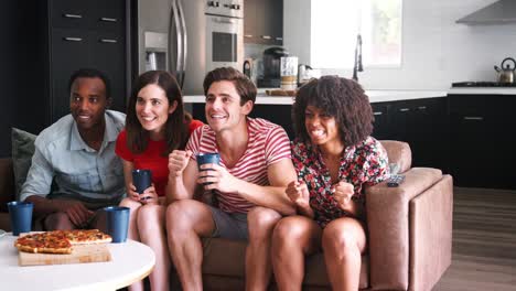 four young adult friends watching sports on tv celebrating