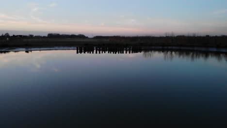 Holzsäulen-Spiegeln-Sich-In-Der-Abenddämmerung-Im-Ruhigen-Fluss-Crezeepolder-In-Der-Nähe-Des-Dorfes-Ridderkerk-In-Den-Niederlanden