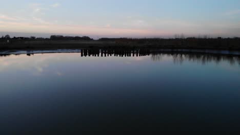 wooden pillars reflected on quiet river at dusk in crezeepolder near the village of ridderkerk in the netherlands