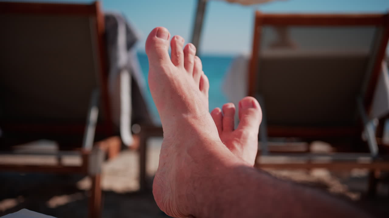 Close up of bare feet resting on a beach lounger with soft sunlight and blurred deck chairs in the background