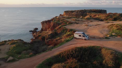 aerial view orbiting campervan parked on praia dos arrifes rocky coastal cliff overlooking scenic atlantic ocean sunrise seascape