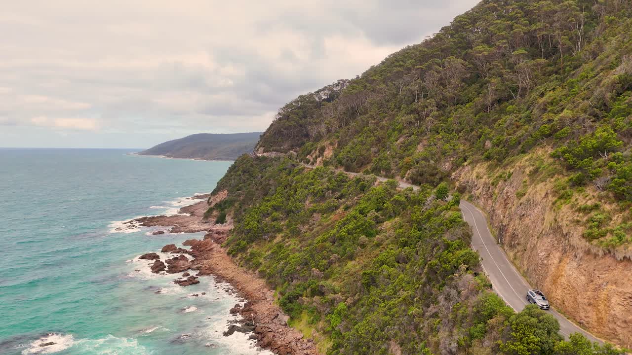 Aerial footage of a car driving along the picturesque Great Ocean Road, showcasing coastal cliffs and vibrant ocean views
