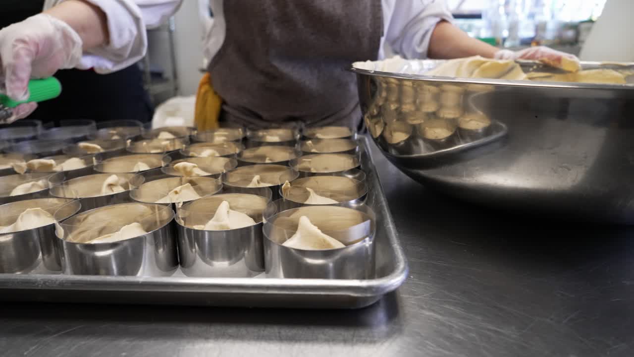Artisan baker precisely scoops cake batter into small round rings, slider close up slow motion 4K