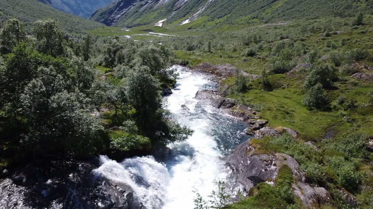 Drone che segue un fiume oltre degli alberi con i fiordi norvegesi sullo sfondo.