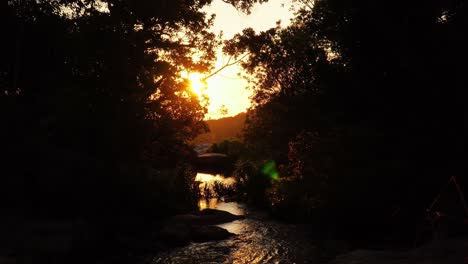 sunset over serene stream, golden light shining on rocks under shade of trees