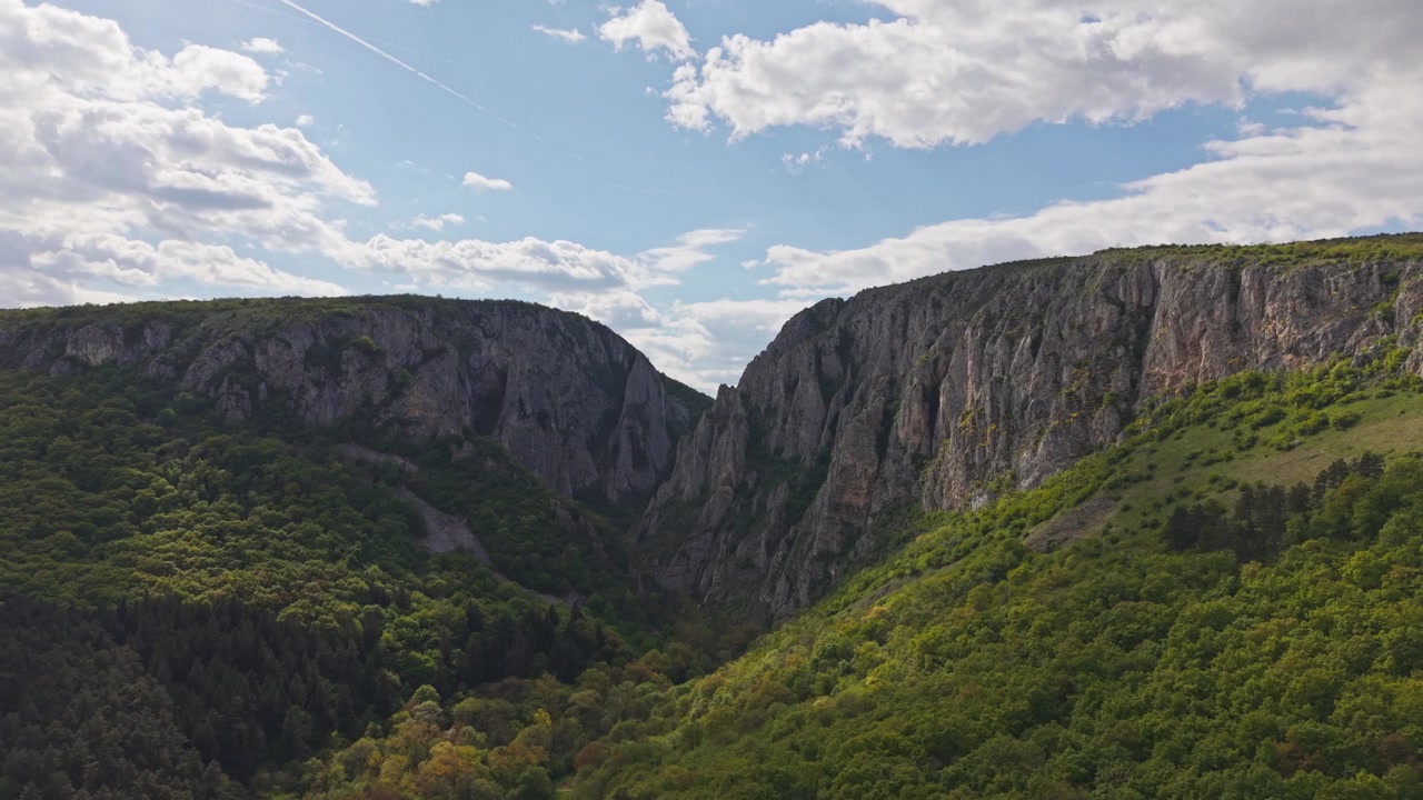 Vídeo aéreo de cânion montanhoso com falésias rochosas e floresta verde.