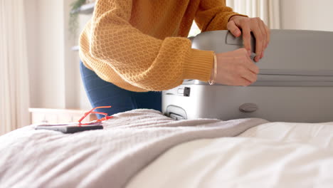 caucasian woman packing and zipping suitcase on bed at home, copy space, slow motion