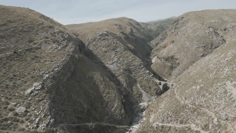 drone shot of the ali pasha bridge outside of gjirokaster, albania on a sunny day sitting in between the rocky mountains with a dry river log