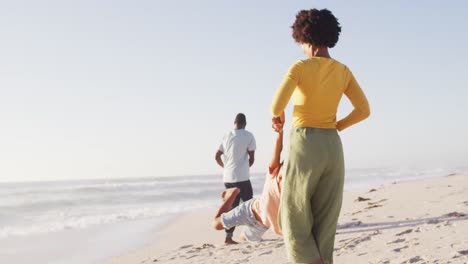 Familia-Afroamericana-Sonriente-Tomándose-De-La-Mano-Y-Jugando-En-La-Playa-Soleada