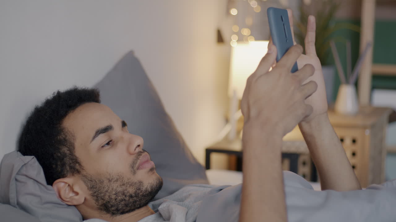 밤에 침대에서 스마트폰을 사용하는 남자