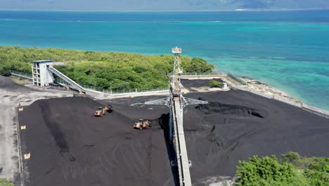 Toma-De-órbita-Aérea-De-Una-Excavadora-En-Funcionamiento-Que-Transporta-Carbón-En-Una-Cantera-De-Mina-De-Carbón-Frente-Al-Océano-Paraíso-En-El-Fondo---República-Dominicana,-Barahona