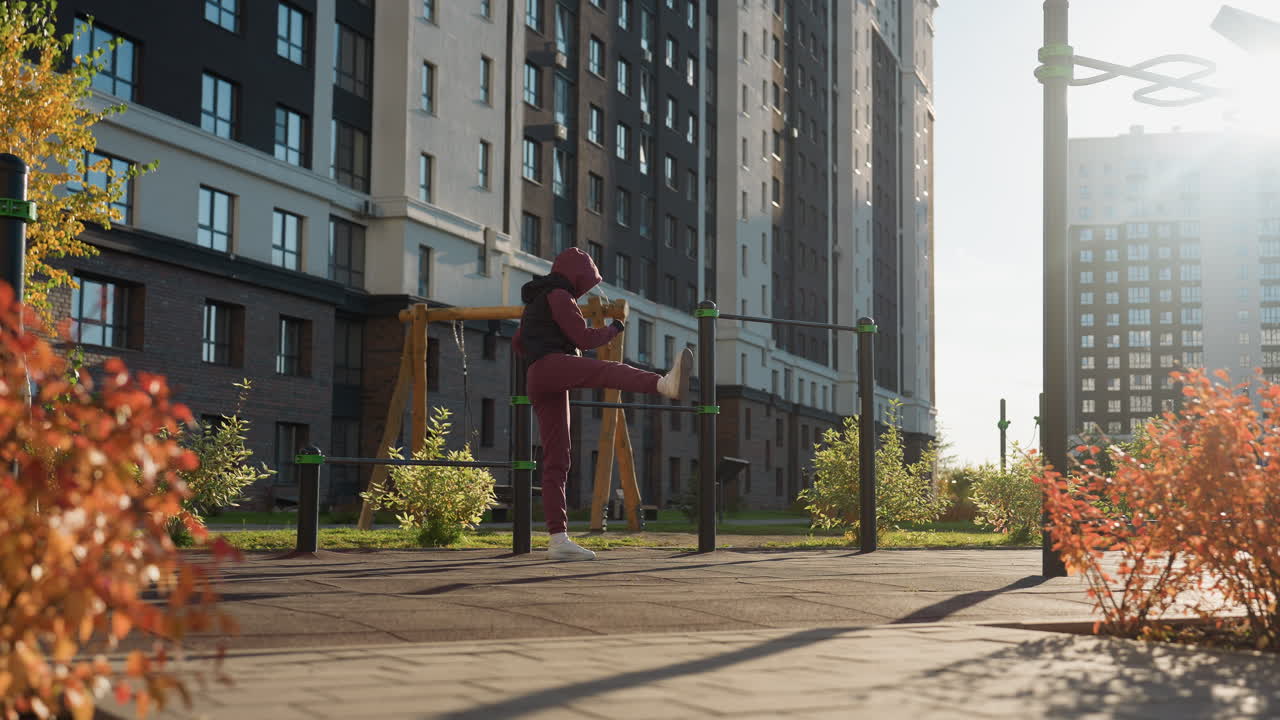 Runner holding pull up bar while lifting legs up and down during intense outdoor workout session under bright sun and skyline wearing hoodie showing strength endurance resilience in urban fitness