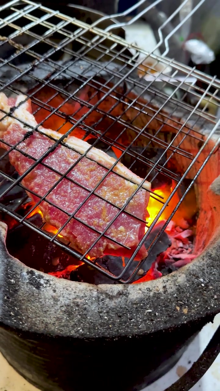 Daging babi yang sudah dimarinasi mendesis di atas panggangan logam di atas arang panas membara dalam tungku