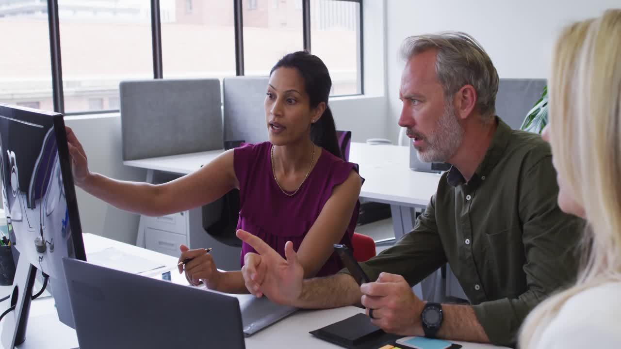 Diverse business colleagues sitting at desk using computer and dicsussing in office