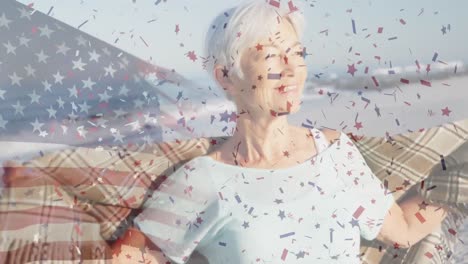 animation of flag of united states of america and confetti over senior caucasian woman on beach