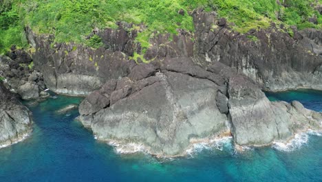 Massive-Coastal-Boulder-and-tropical-island-cliffside-inside-idyllic-ocean-cove---aerial-orbit