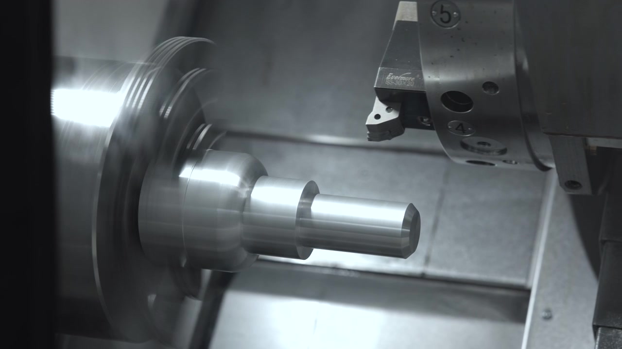 Albero metallico lucidato che ruota all'interno di una macchina per lavorazioni di precisione mentre un utensile da taglio lavora nelle vicinanze, con un involucro scuro, superfici in acciaio riflettenti, luce grigia fredda, forti riflessi e messa a fuoco