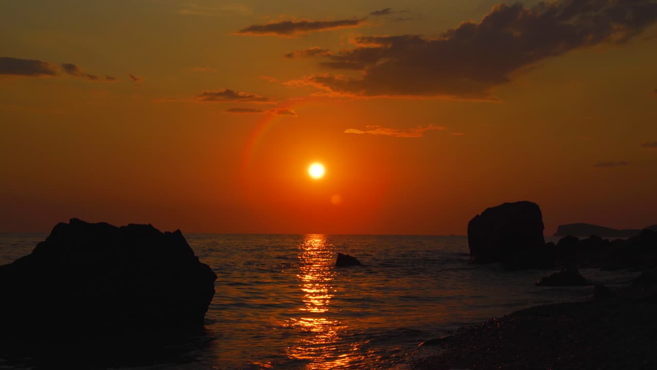 절벽 실루엣을 통해 활기찬 바닷물에 반사되는 다채로운 하늘에 태양이 빛나는 일몰 벽지