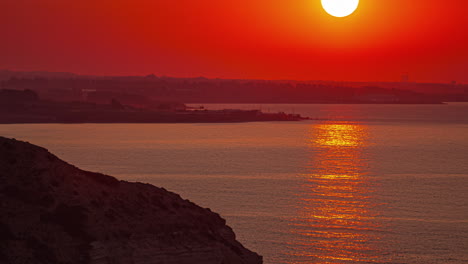 the sun rises from behind an island into a fiery sky reflecting on the water