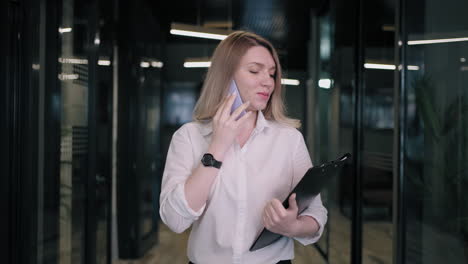 a blonde business woman walks down the corridor and talks on the phone with a client