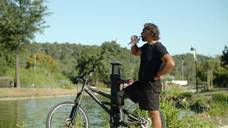 Long shot of man with bionic leg drinking water after cycling