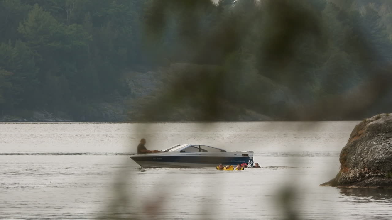 Bambini si tuffano da una barca a motore nell'acqua del lago con il resto della famiglia in una calda giornata estiva per rinfrescarsi, ripresa con teleobiettivo.